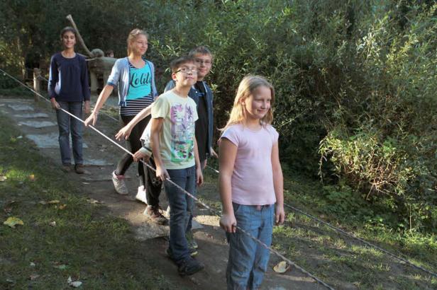 Eine Gruppe Kinder balanciert auf einem Seil im Freien.