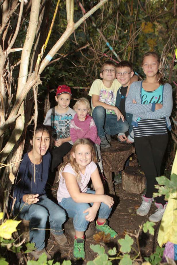 Eine Gruppe Kinder sitzt in einer selbstgebauten Hütte im Wald.