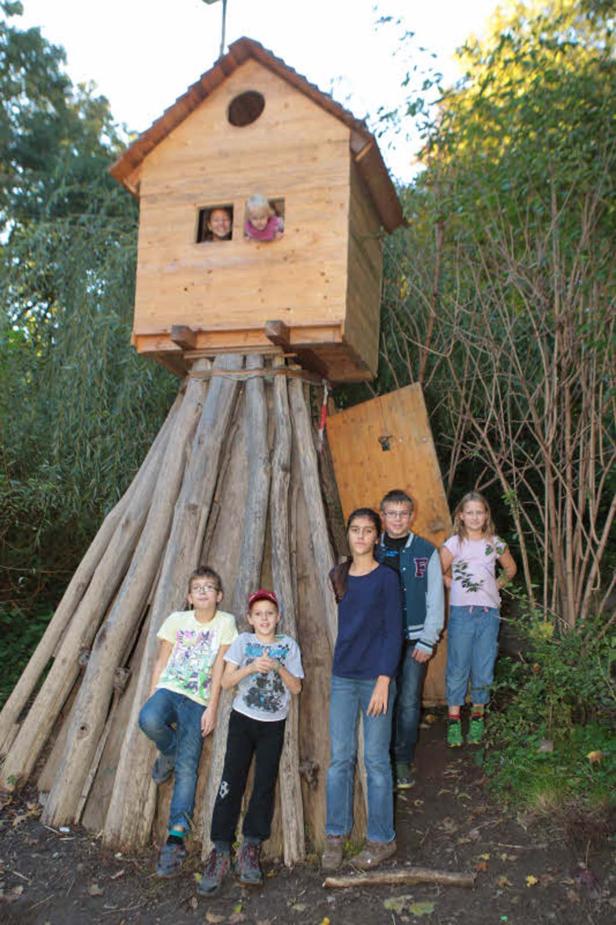 Eine Gruppe von Kindern steht vor einem Baumhaus auf Stelzen.