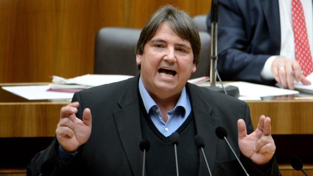Ein Mann gestikuliert während einer Rede vor mehreren Mikrofonen.
