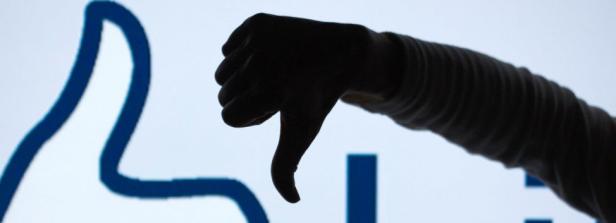 Eine Hand gibt vor einem Like-Symbol den Daumen nach unten.