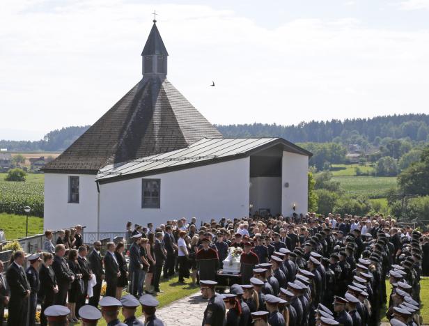 Eine Trauergemeinde versammelt sich vor einer Kirche auf dem Land.