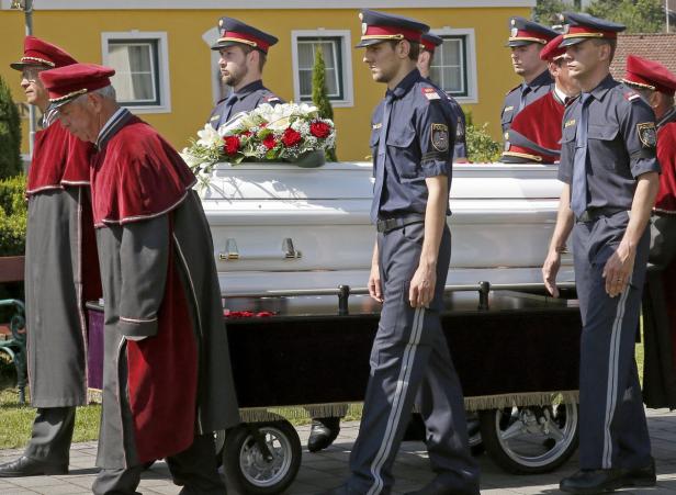 Polizisten und Geistliche begleiten einen Sarg mit Blumenschmuck.