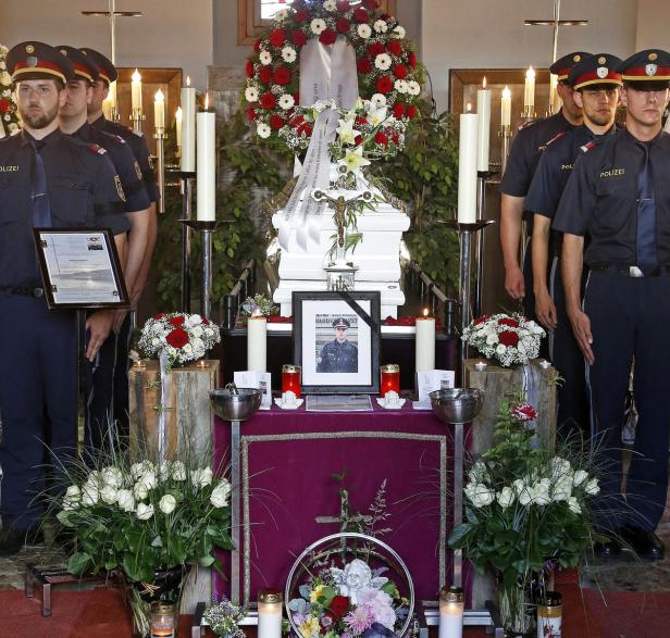 Polizisten stehen Wache an einem mit Blumen geschmückten Sarg und einem Porträt des Verstorbenen.