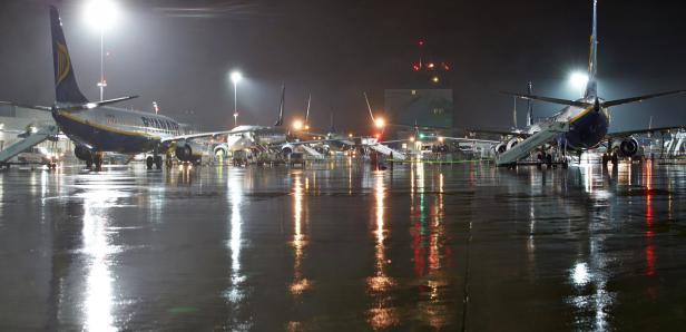 Mehrere Ryanair-Flugzeuge stehen nachts auf einem regennassen Rollfeld.