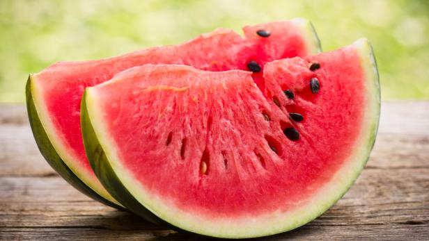 Zwei saftige Wassermelonenspalten liegen auf einem Holztisch.