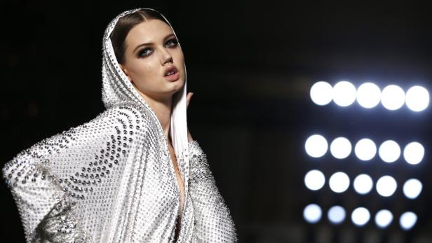 Ein Model mit Kapuze und einem mit Pailletten besetzten Kleid auf dem Laufsteg.