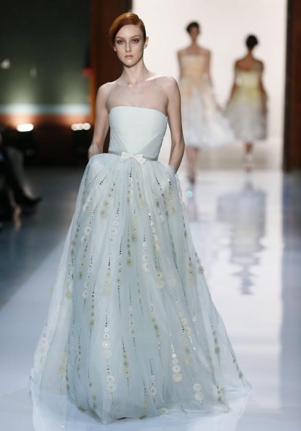 Eine Frau in einem hellblauen, trägerlosen Kleid mit Schleife und kreisförmigen Verzierungen auf einem Laufsteg.