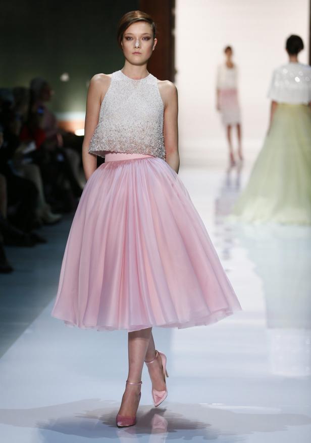 Ein Model präsentiert ein rosafarbenes Kleid mit einem verzierten Oberteil auf dem Laufsteg.