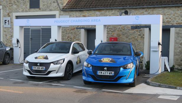 Ein weißer und ein blauer Peugeot 208 parken an einer Ladestation.