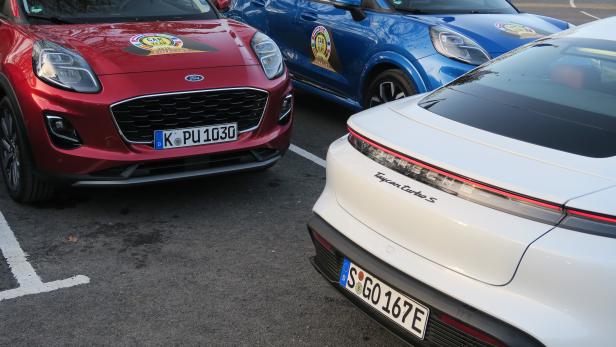 Ein roter Ford, ein blauer Ford und ein weißer Porsche parken nebeneinander.