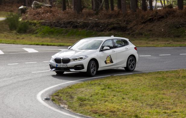 Ein weißer BMW 1er fährt auf einer kurvenreichen Straße.