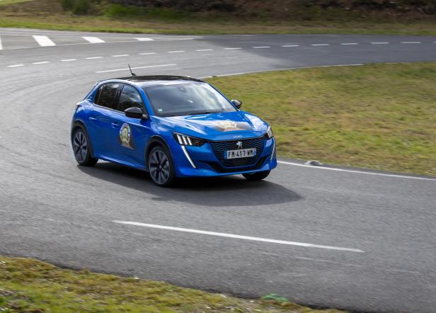 Ein blauer Peugeot 208 fährt auf einer kurvenreichen Straße.