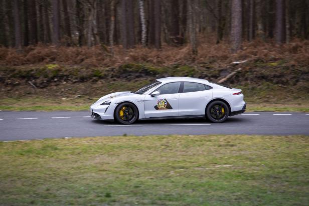 Ein weißer Porsche Taycan fährt auf einer Straße durch einen Wald.