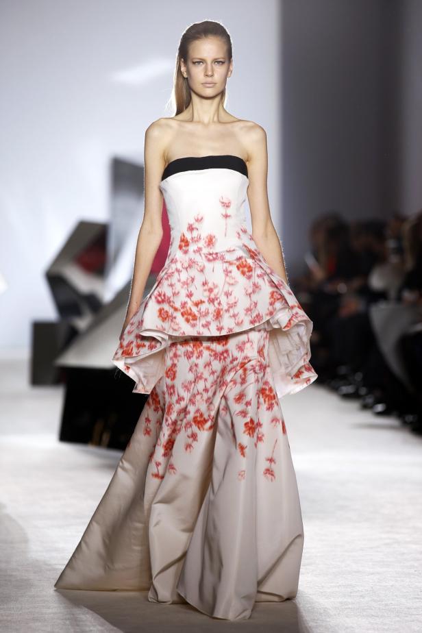 Ein Model präsentiert ein trägerloses, weißes Kleid mit rotem Blumenmuster auf dem Laufsteg.