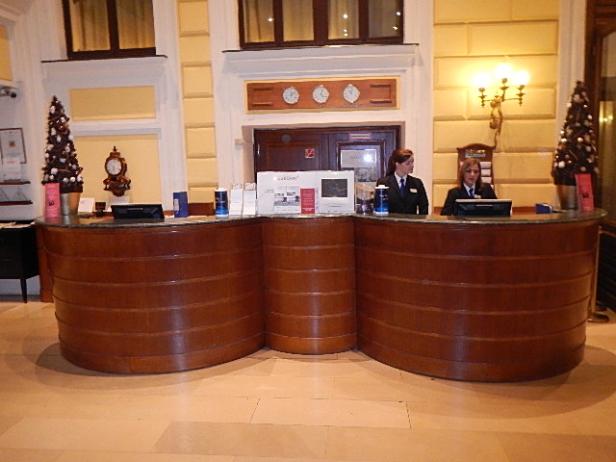 Zwei Angestellte stehen hinter einem halbrunden Empfangstresen in einem Hotel.