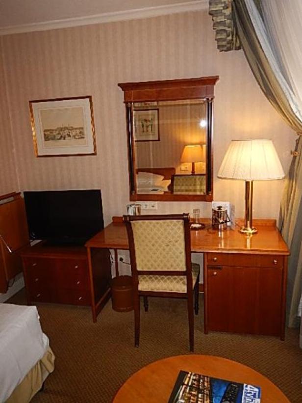 Ein Schreibtisch mit Stuhl, Lampe und Fernseher in einem Hotelzimmer.