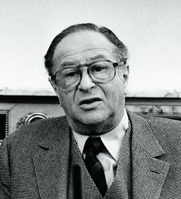 Bruno Kreisky trägt eine Brille, ein gemustertes Sakko sowie eine Krawatte und blickt ernst in die Kamera.
