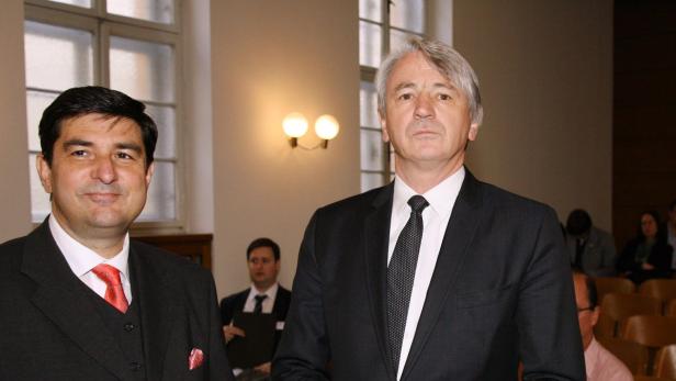 Zwei Männer in Anzügen stehen in einem Raum.