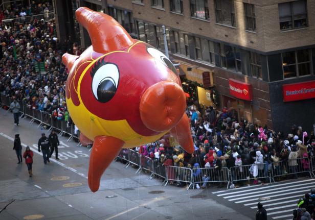 Ein großer, roter und gelber Fisch-Ballon schwebt über eine Menschenmenge in einer Stadt.