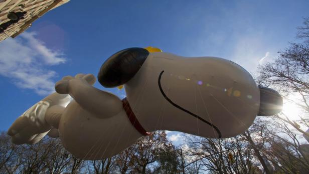 Ein Snoopy-Ballon fliegt vor blauem Himmel und Baumwipfeln.
