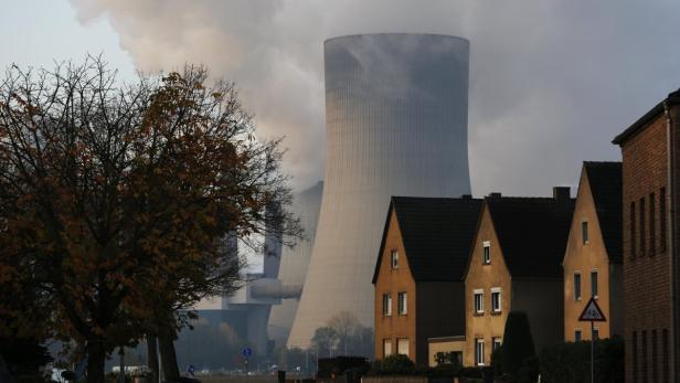 Ein Kohlekraftwerk steht hinter Wohnhäusern in einer Vorstadtsiedlung.