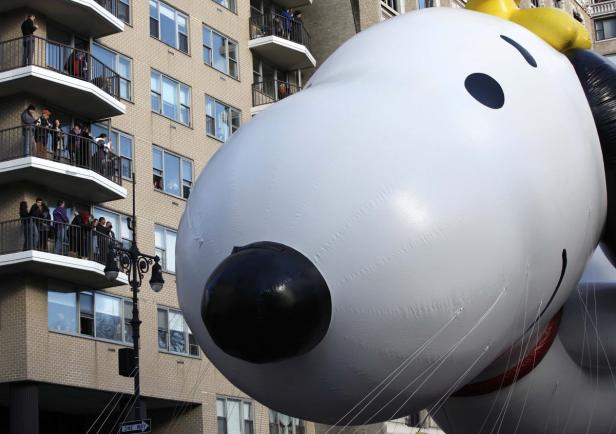Ein riesiger Snoopy-Ballon schwebt vor einem Wohnhaus, von dessen Balkonen Menschen zusehen.
