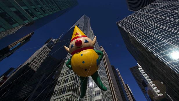 Ein Clown-förmiger Ballon schwebt zwischen Wolkenkratzern.