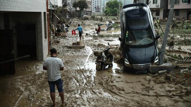 Nach einem Hochwasser stehen Autos und Motorroller in einer schlammigen Straße.