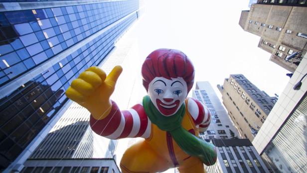 Eine Ronald McDonald-Figur schwebt bei einer Parade zwischen Hochhäusern.