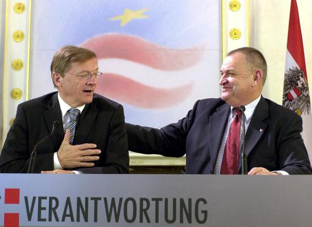 Zwei Männer in Anzügen sitzen an einem Tisch mit der Aufschrift „Verantwortung“.