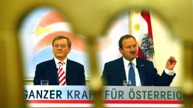 Zwei Männer sitzen vor einer österreichischen Flagge und einem Banner mit der Aufschrift „Ganzer Kraft für Österreich“.