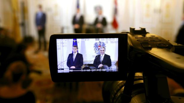 Eine Videokamera filmt zwei Männer vor Flaggen bei einer Pressekonferenz.