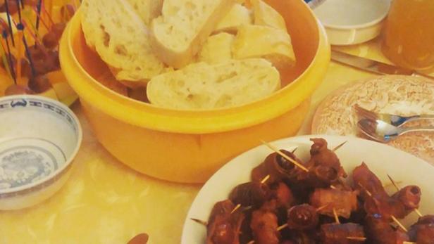 Ein Tisch mit Brot in einem gelben Behälter und Datteln im Speckmantel auf einem Teller.