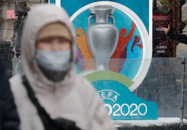 A person wearing a protective face mask walks past the Euro 2020 countdown clock in central Saint Petersburg