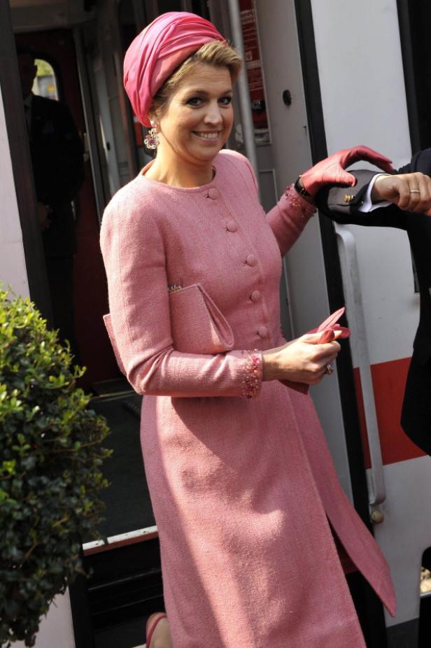 Königin Máxima verlässt einen Zug in einem rosa Tweed-Kostüm und passendem Turban.