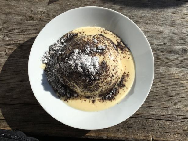 Ein Germknödel mit Vanillesauce und Puderzucker auf einem Teller.