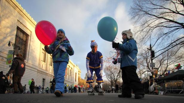 Kinder mit Ballons und ein Mann auf Rollschuhen nehmen an einer Parade teil.