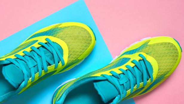 Ein Paar gelb-türkise Laufschuhe auf einem rosa und hellblauen Hintergrund.