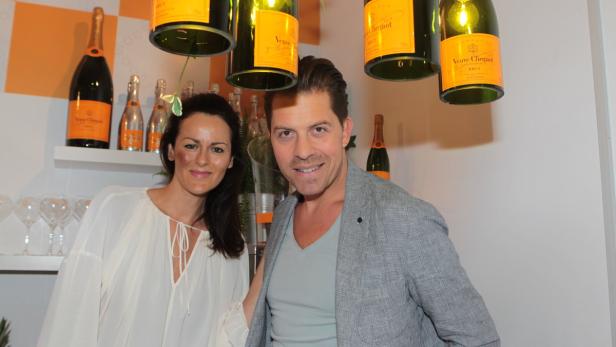 Eine Frau und ein Mann posieren vor einer Wand mit Veuve Clicquot Champagnerflaschen.