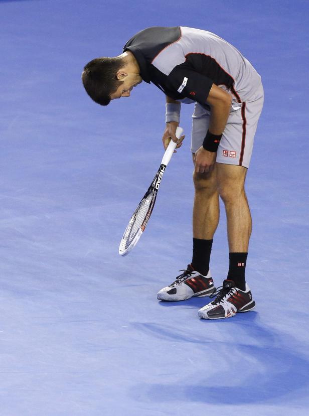 Ein Tennisspieler blickt mit gesenktem Kopf auf seinen Schläger auf dem Platz.