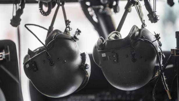 Zwei olivgrüne Helikopterhelme hängen an Haken.