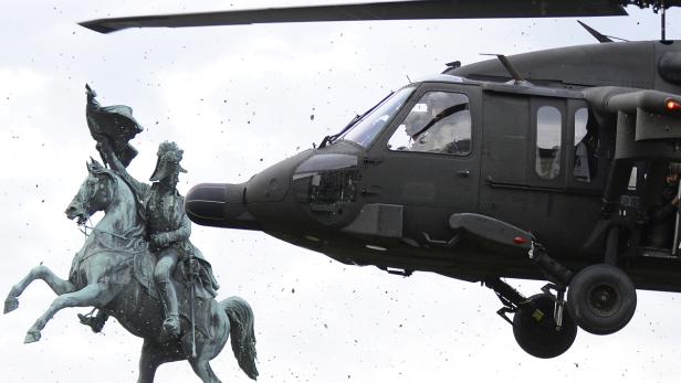 Ein Hubschrauber fliegt nahe einer Reiterstatue, wodurch Staub aufgewirbelt wird.