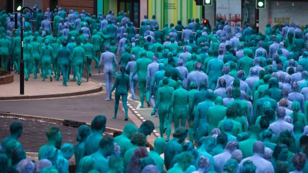 Hunderte blau und grün bemalte Menschen überqueren eine Straße.