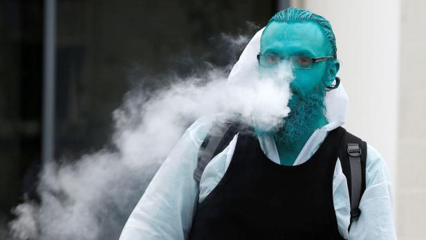 Ein Mann mit blau gefärbtem Gesicht und Bart atmet Dampf aus.