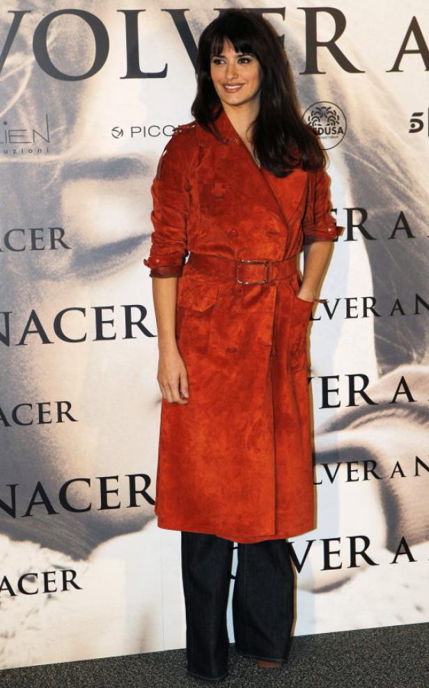 Penélope Cruz trägt einen orangefarbenen Mantel vor einem „Volver“-Filmposter.