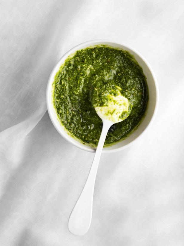 Ein Schälchen Pesto mit einem Löffel auf einem weißen Tuch.