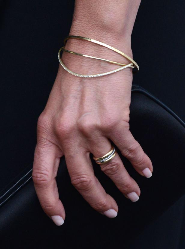 Die Hand einer Frau mit goldenen Armreifen und einem Ring vor einem schwarzen Hintergrund.