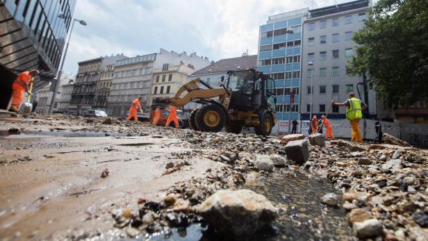 Bauarbeiter und ein Bagger räumen Geröll von einer Straße in der Stadt.