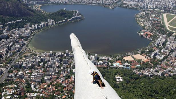 Ein Arbeiter auf dem Arm der Christusstatue in Rio de Janeiro mit Blick auf die Stadt.